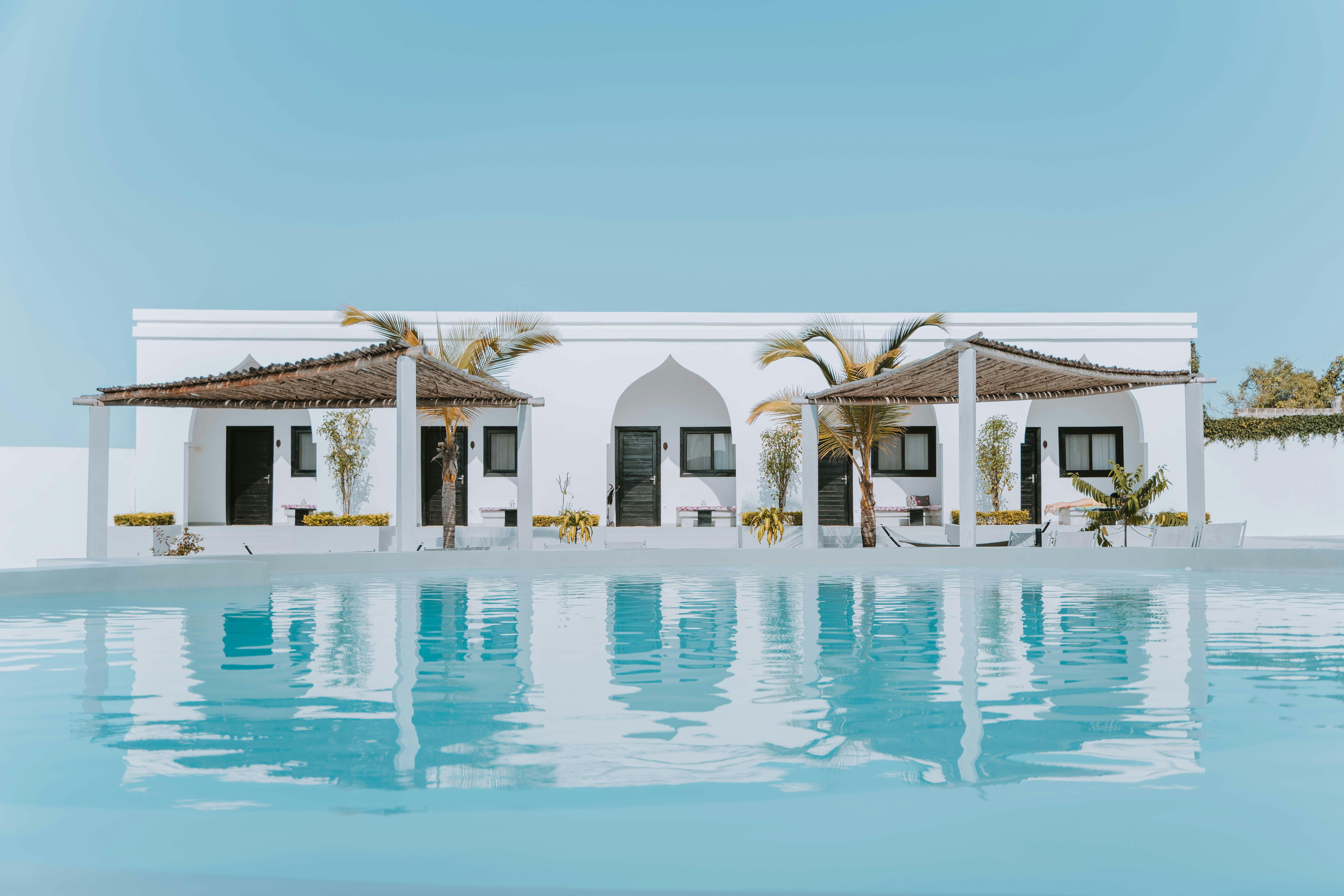 Modern white villa with arched doorway and palm trees reflected in a clear turquoise swimming pool under a bright blue sky Zanzibar.