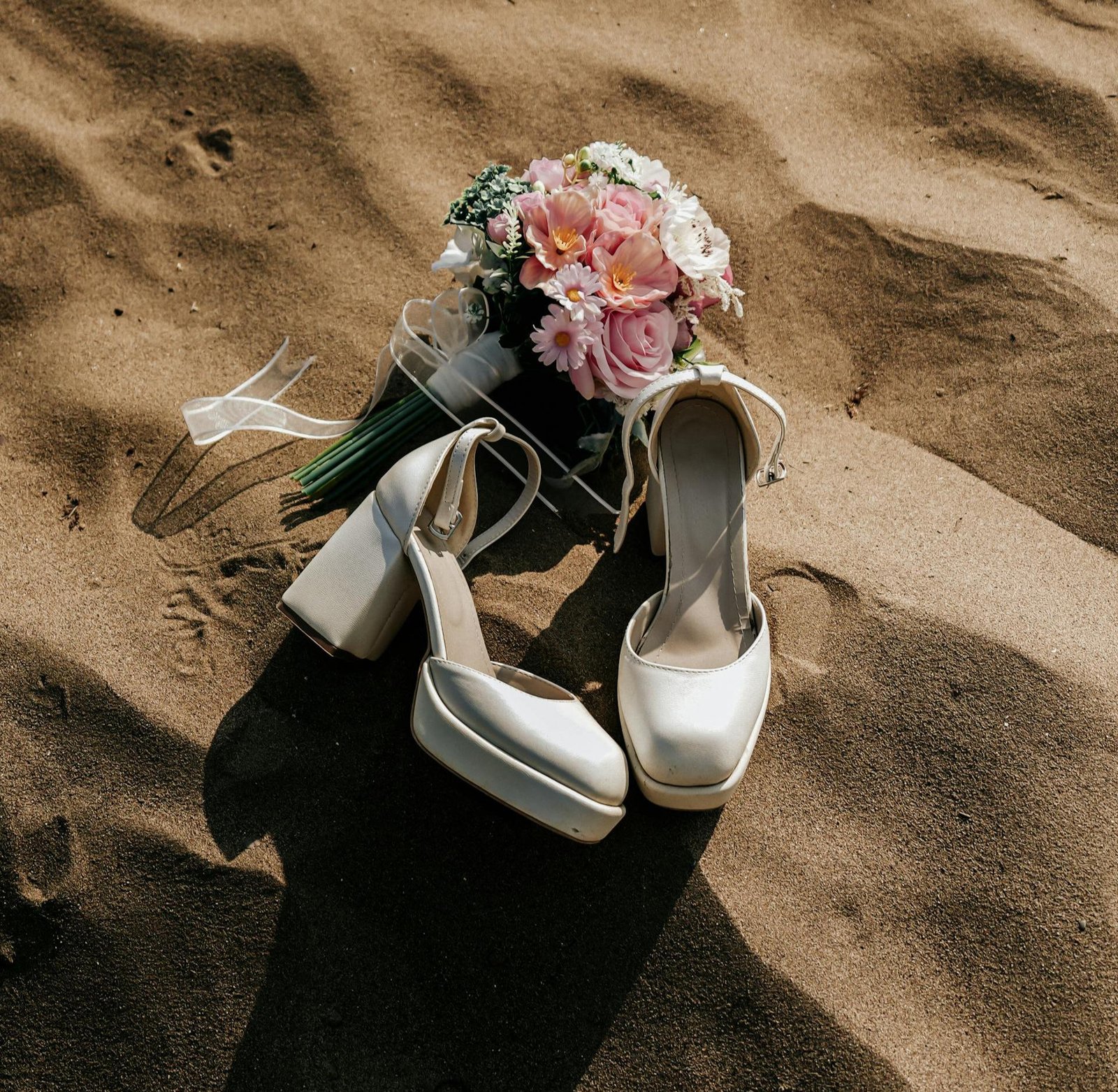 Elegant bridal shoes and a bouquet on a sandy beach.